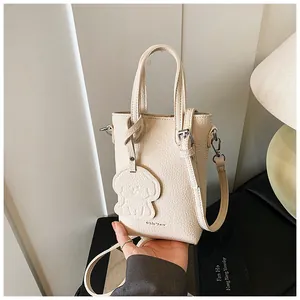 Dettaglio della borsa beige con motivo litchi, ciondolo a cane e tracolla rimovibile