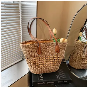 Detail of straw woven tote bag featuring brown leather handles and natural fiber texture