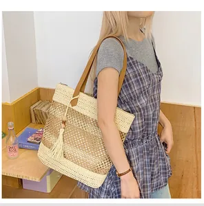 Detail of hollow woven straw tote bag featuring contrast stitching and stylish beige tassel