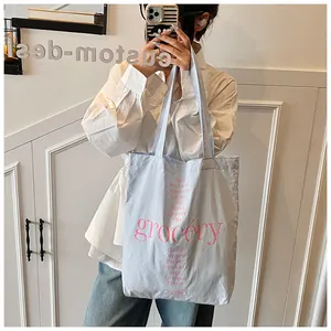 Detalle del bolso tote de lona con estampado grocery rosa y texto floral sostenido por modelo