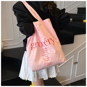 Bolso tote de lona rosa con letras rojas mostrado por una modelo en un entorno casual