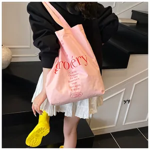 Detalle del bolso tote de lona rosa con texto grocery rojo y lista de hierbas al hombro