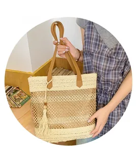 Detail of woven straw tote bag featuring brown leather handles and decorative tassel