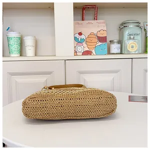 Detailed close-up of brown woven straw tote bag with leather handles on a white table