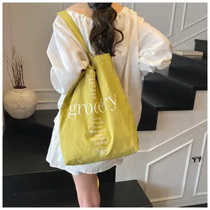 Bolso tote de lona amarilla con estampado grocery blanco usado como bolso de hombro