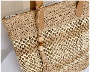 Detailed view of hollow straw tote bag with brown leather handles and tassel charm