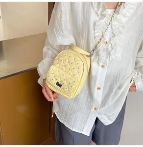 Detail showing a yellow quilted mini backpack with rhinestones and chain strap worn by a model