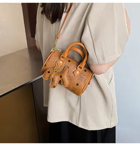 Detail of tan Boston bag with monogram print and dog charm worn by a female model