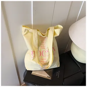 Detalle del bolso tote de lona amarillo pastel con texto rosa de hierbas en una silla negra