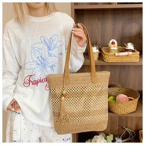 Detail of hollow woven straw tote bag featuring leather handles and tassel pendant