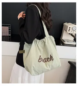 Bolso tote de nailon verde claro con texto Beach llevado por modelo en una cafetería