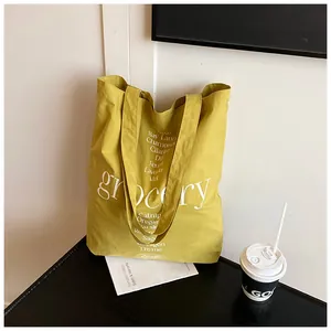 Detalle de bolsa tote de lona amarilla con texto blanco grocery y diseño de hierbas