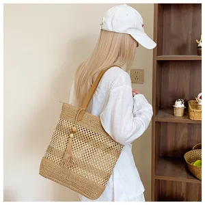 Detail of hollow-out straw tote bag with long tassel and brown leather shoulder strap