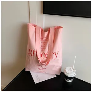 Detalle del bolso tote de lona rosa con texto grocery rojo y lista de hierbas