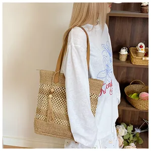 Detail of hollow woven straw bag with tassels and brown leather handle for summer beach