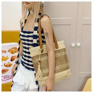 Detail of hollow woven straw tote bag with brown leather handles and fringe tassel