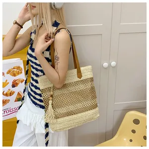 Detail of hollow woven straw tote bag featuring beige tassels and dark brown leather handles