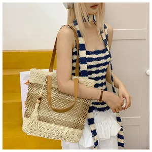 Detail of hollow-out woven straw tote bag with brown leather handles and fringe tassel
