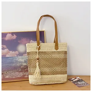Detail of hollow woven straw tote bag featuring brown leather handles and tassel charm