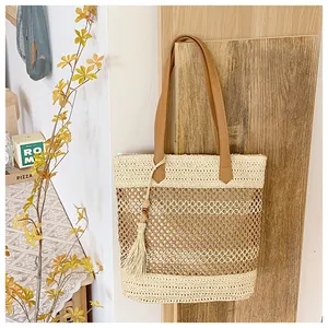 Close-up of bohemian woven straw tote bag with brown leather handles and tassel detail
