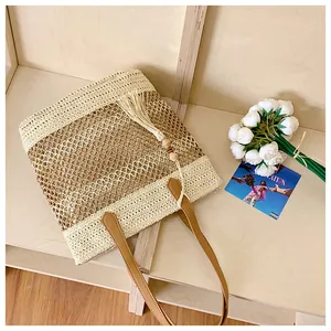 Detail of hollow woven straw tote bag with brown leather handles and tassel accent