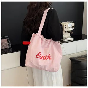 Detalle de bolso tote de nailon rosa con bordado Beach rojo y cierre de cordón al hombro