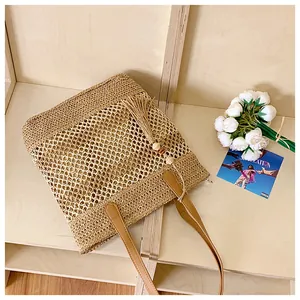 Detail of hollow-out mesh straw tote with brown leather handles and wooden bead tassel