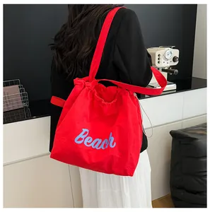 Detalle del bolso tote de nailon rojo con texto Beach azul y cierre de cordón ajustable