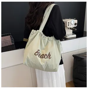 Detalle del bolso tote verde claro con cordón, estampado Beach y correa ancha