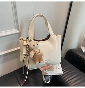 Detail der cremefarbenen PU-Leder Handtasche mit Bärenanhänger und Logoprägung