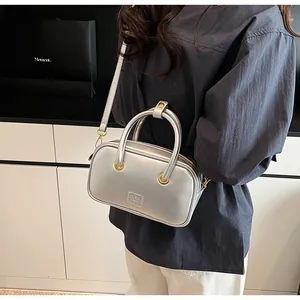 Detail of silver crossbody bag with golden ring handles and embossed logo on the front
