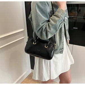 Detailed shot of a black leather crossbody bag with golden rings and logo on casual outfit