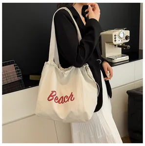 Detalle del bolso tote de lona crema con estampado Beach rojo y cierre con cordón