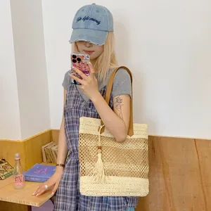 Hollow straw shoulder bag with tassels and brown leather straps for beach vacation