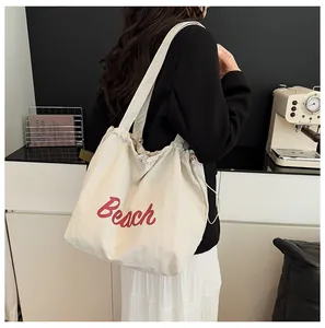 Detalle del bolso tote de nailon crema con letras Beach rojas y cierre con cordón