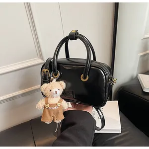 Detail of black patent leather handbag featuring shiny finish and cute bear charm pendant
