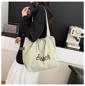 Detalle del bolso tote verde claro con cordón e impresión Beach al hombro