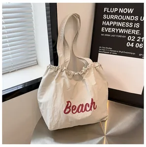 Primer plano del bolso tote beige con texto Beach en rojo sobre una mesa de metal