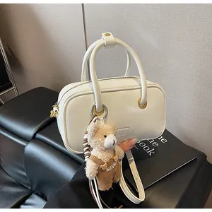 Detail of a beige leather handbag featuring a cute plush bear charm on a black bench