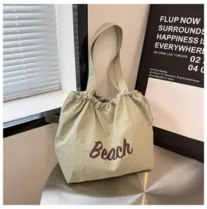 Detalle de bolso tote de lona verde con bordado Beach y cierre de cordón ajustable