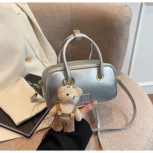 Detail of silver square handbag with metallic texture and cute teddy bear charm