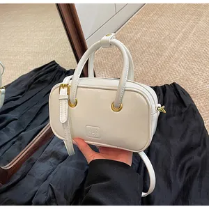 Close-up of a white Boston bag with gold hardware and embossed logo on a leather surface