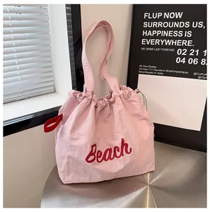 Detalle del bolso tote de lona rosa con cordón, letras Beach rojas y correa lateral fina