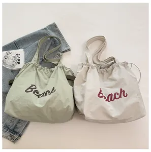 Detalle de bolsos tote grandes de nailon con cordón y estampado Beach en crema y verde