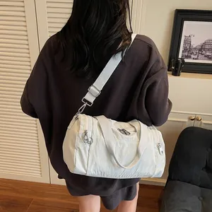 White nylon barrel bag with adjustable strap shown on model in a casual outdoor setting
