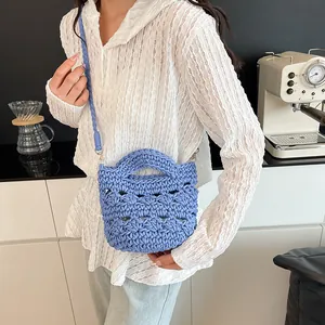 Blaue handgewebte Häkeltasche mit zwei Griffen und langem Gurt in legerer Lifestyle-Umgebung
