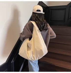 Model wearing a large beige nylon tote bag with a slouchy design and adjustable strap