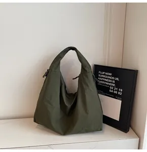 Macro detail of dark green nylon tote bag showing textured fabric on white marble surface