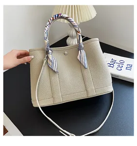 Dettaglio della borsa tote beige con trama litchi, sciarpa in seta e bottone a pressione