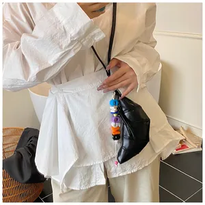 Detail der schwarzen glänzenden Croissant-Tasche mit Kontrastnaht und Perlenanhänger